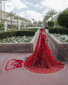 a woman in a red bridal gown stands on a stone wall near flowers and bushes