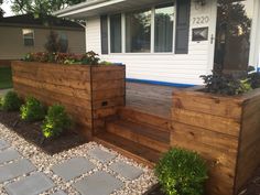 a wooden planter sitting on the side of a house next to a stone walkway