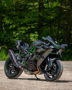 a black and green motorcycle parked on the side of a road next to some trees