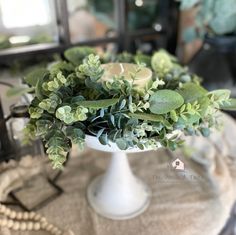 a white vase filled with green plants sitting on top of a table next to a mirror