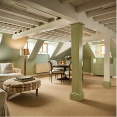 A cozy attic living space with green-painted beams, a dining table, sofa, armchairs, and warm lighting.