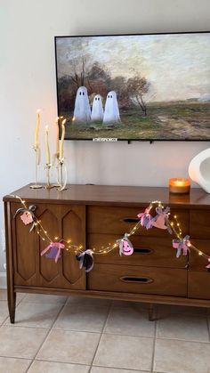 a tv mounted on the wall above a wooden dresser with candles and decorations in front of it