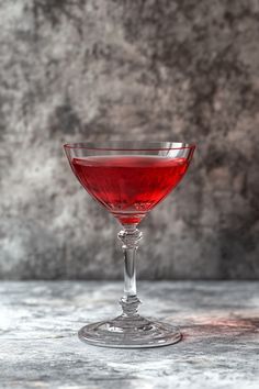 a glass filled with red liquid sitting on top of a table next to a wall