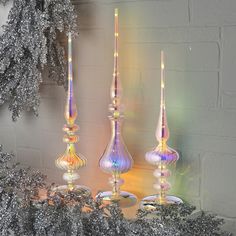 three glass candlesticks sitting on top of a table next to a christmas tree