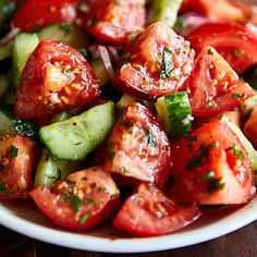 a white plate topped with cucumber and tomato salad on top of a wooden table