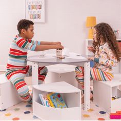 two children sitting at a table playing with each other in their playroom, while one child sits on the floor