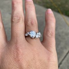 a person's hand holding an engagement ring with three stones on it and the middle finger