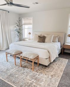 a large white bed sitting in the middle of a bedroom next to a window with curtains