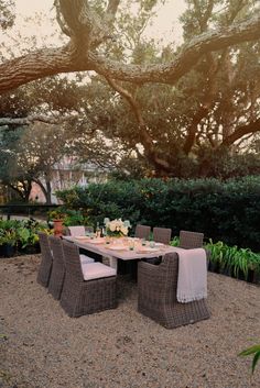 an outdoor dining table and chairs in the middle of a gravel area under a large tree