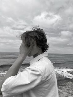 a man standing on top of a beach next to the ocean holding his hand up to his face