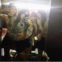 four women taking pictures in front of a mirror with their cell phones and lights on