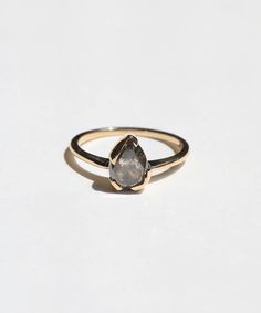 a gold ring with a grey diamond on the front and side, sitting on a white surface