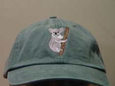 a green hat with a koala on it is hanging from a tree branch in front of a white wall