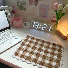 a laptop computer sitting on top of a desk next to a clock and flower vase