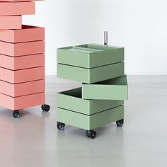 two different colored boxes on wheels in an empty room, one is pink and the other is green