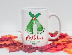 a white coffee mug with two green bells on it and the words mistletes written in red