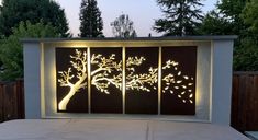 an outdoor area with a tree and lights on the wall, in front of a fence