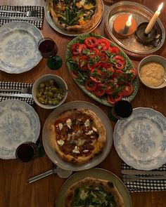 a table topped with plates and bowls filled with food next to a pizza on top of a wooden table