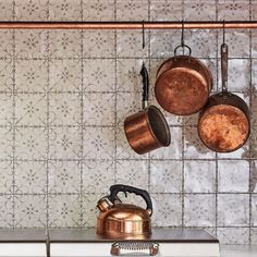 copper pots and pans hanging on the wall above a stove with a tea kettle