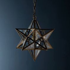 a glass star hanging from a chain against a blue sky with light shining on it