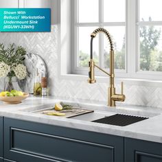 a kitchen sink under a window next to a counter top with fruit and flowers on it