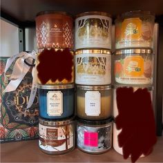 many different types of candles are sitting on a shelf next to a box with a bow