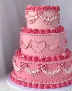 a three tiered cake with pink icing and hearts on it's sides