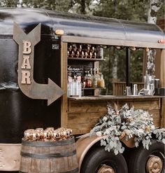 an old fashioned bar cart is decorated with greenery and wooden barrels as well as flowers