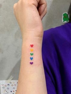 a woman with a colorful heart tattoo on her left arm and the word love spelled in small hearts