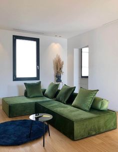 a living room filled with green couches and pillows on top of a hard wood floor