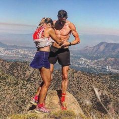 a man and woman standing on top of a mountain looking out at the city below