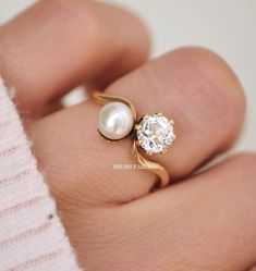 a woman's hand holding a pearl and gold ring