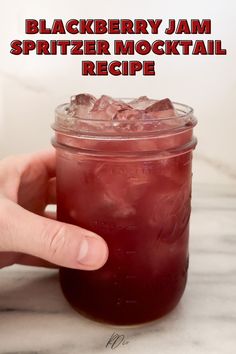 a hand holding a mason jar filled with blackberry jam spritzer mocktail recipe