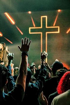 people raising their hands up in front of a cross on a stage with bright lights