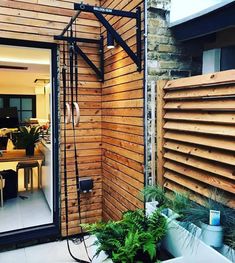 an outdoor shower in front of a wooden wall with plants on the floor and potted plants next to it