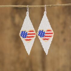 pair of earrings with american flag design on them hanging from a line against a wooden background