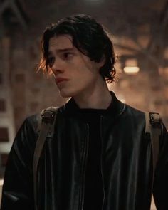 the young man is wearing a black leather jacket and looking off into the distance with his hands in his pockets