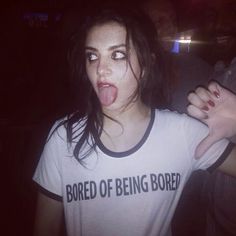 a woman sticking her tongue out while wearing a t - shirt that says bored of being bored