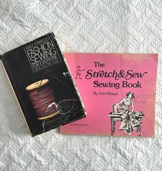 two books sitting on top of a bed next to each other, one has a spool of thread