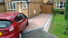 a red car parked in front of a brick driveway next to a house with two windows