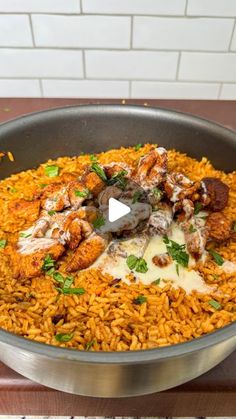 a pan filled with rice covered in meat and sauce on top of a wooden table