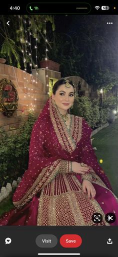 a woman in a red and gold dress sitting on a bench with lights strung from the trees behind her