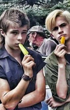 two young men standing next to each other holding bananas and looking at something in their hands