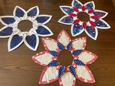 three red, white and blue paper flowers sitting on top of a wooden table next to each other