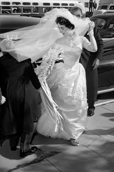 a woman in a wedding dress walking down the street with her veil over her head