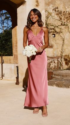 a woman in a long pink dress holding a bouquet of white flowers and smiling at the camera