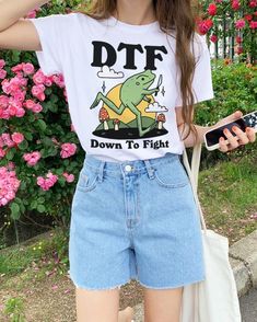 a woman wearing shorts and a dtf t - shirt is holding her cell phone