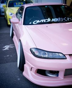 a pink car parked in front of a yellow car with the word on it's hood