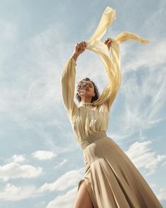 a woman in a long dress is holding a yellow scarf up to her head with both hands