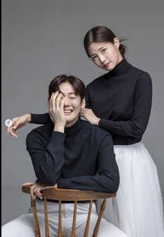 a man sitting on top of a wooden chair next to a woman who is touching her face